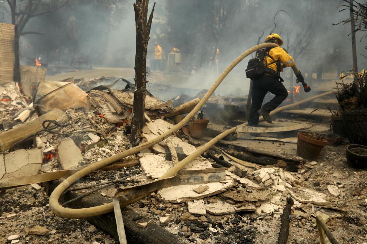 A firefighter carries a hose back to his rig while walking through a destroyed home in Pacific Palisades.