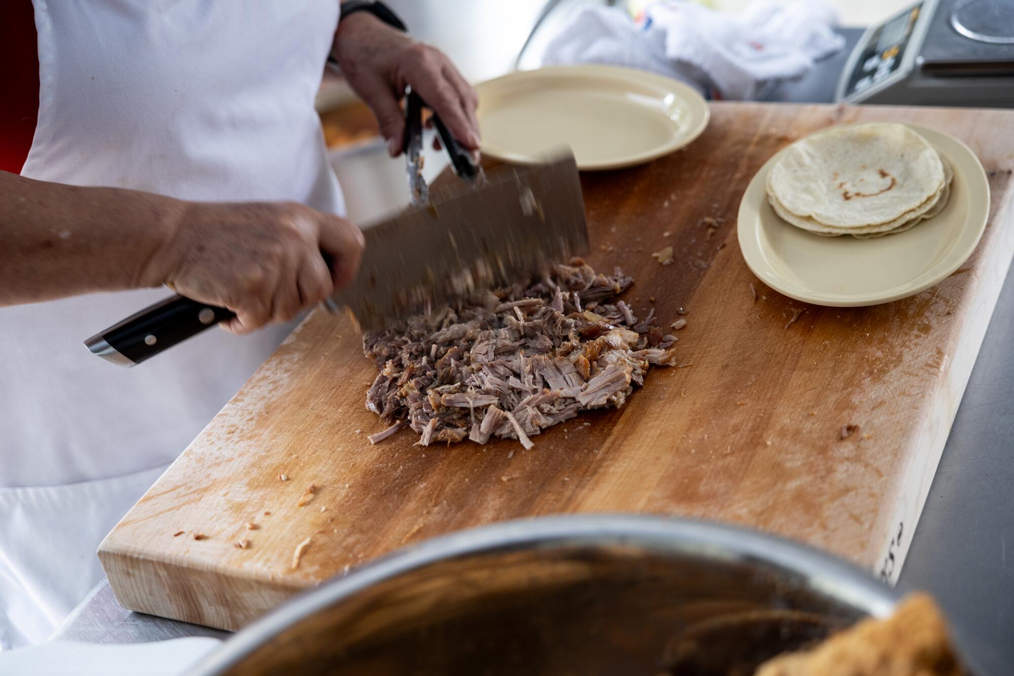 A man chops meat on a cutting board.