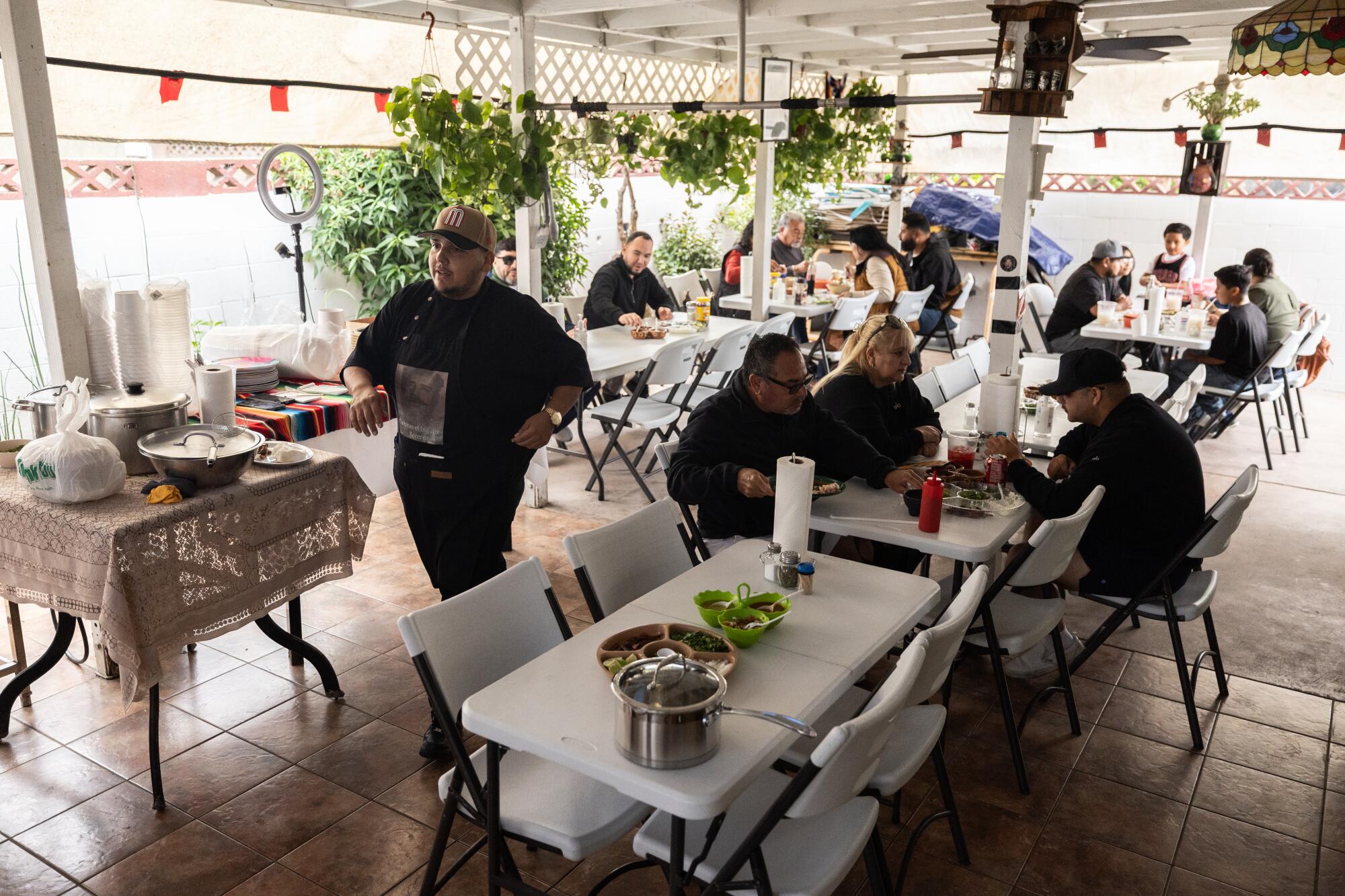 Roberto Preciado Jr. walks between tables in the dining area located in the backyard.