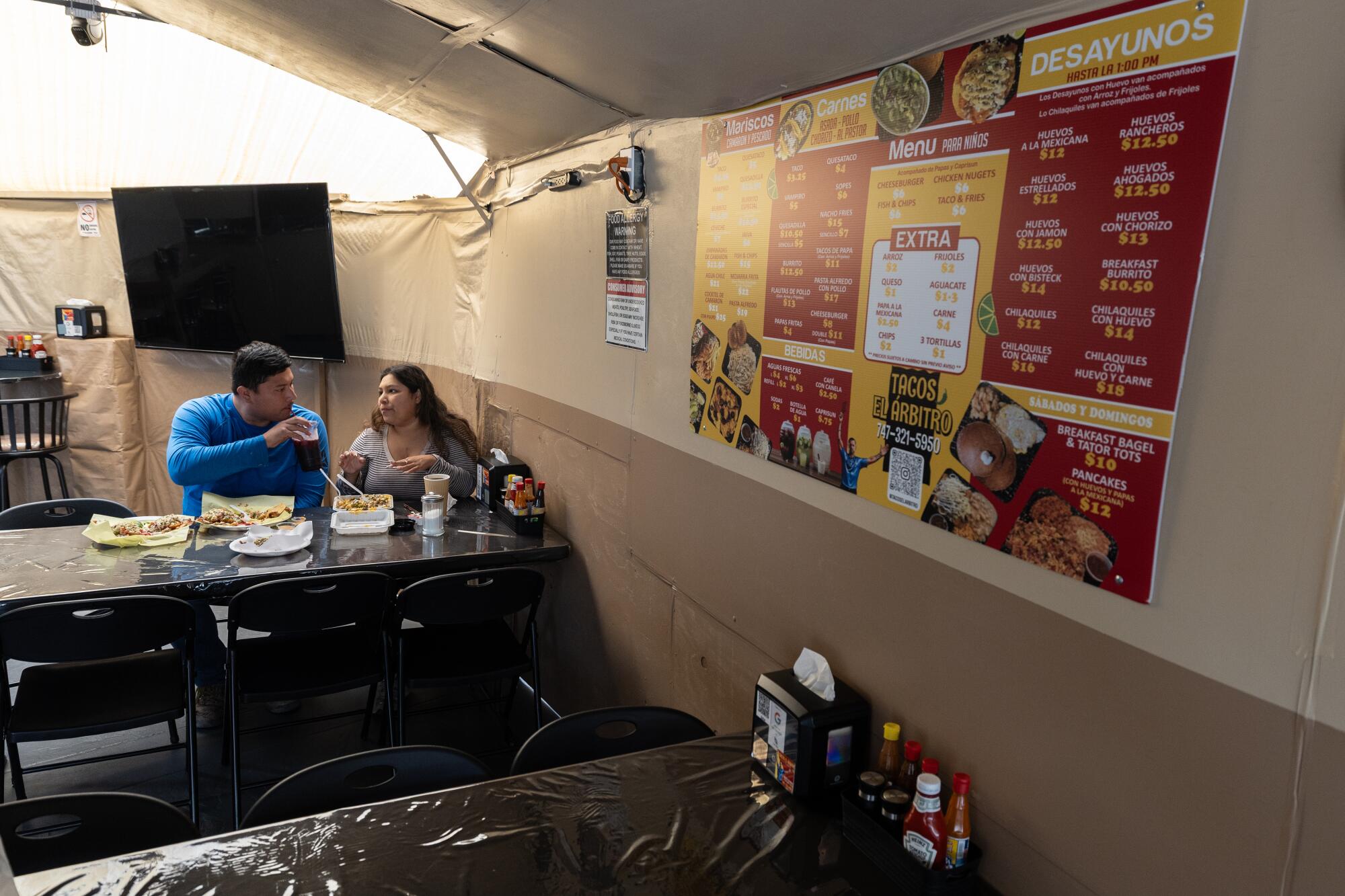 Customers Esmeralda and Omar eat outdoors under a large tent at Tacos El Arbitro in Arleta.