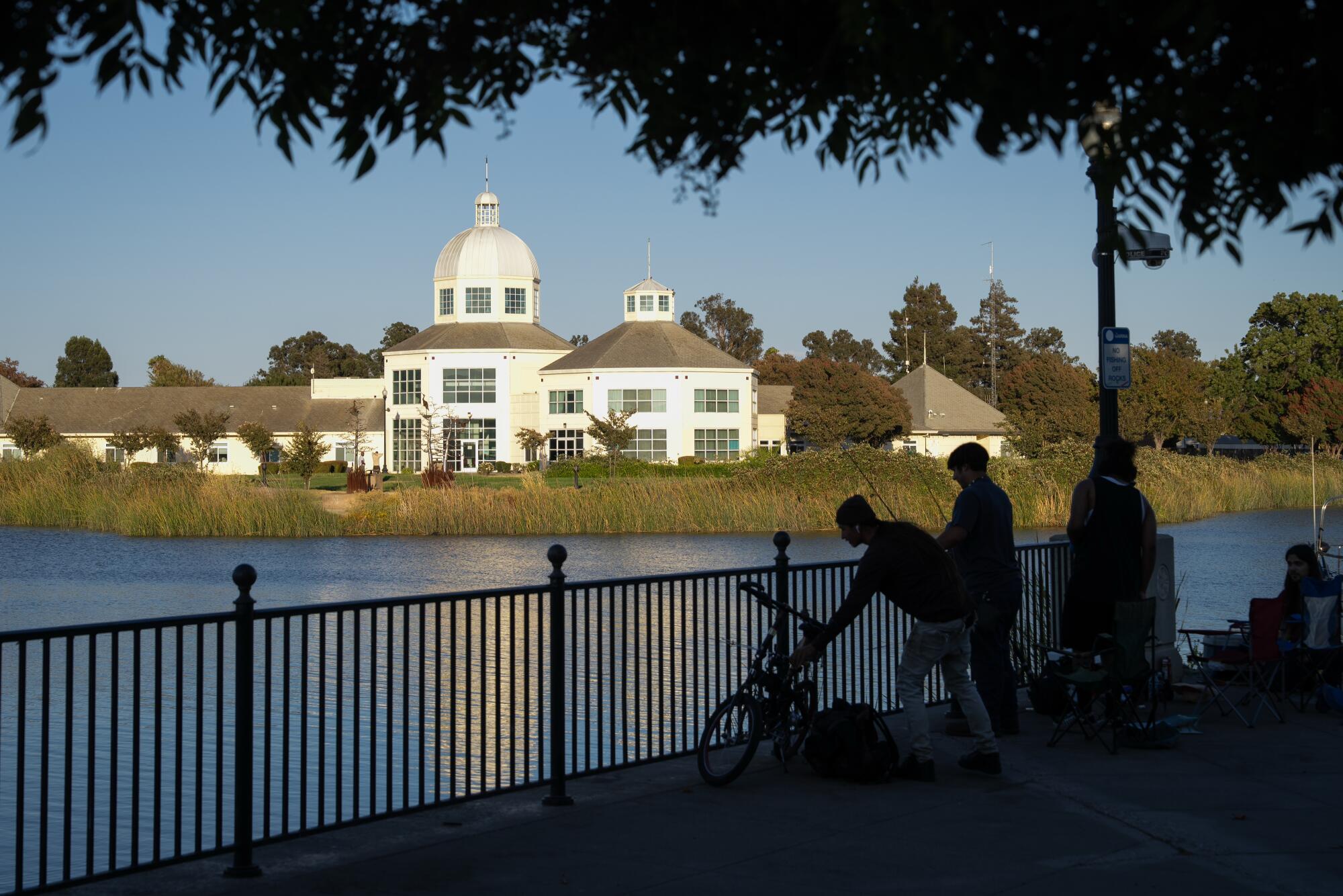 Several people in silhouette fishing near a riverbank, a domed building in the distance