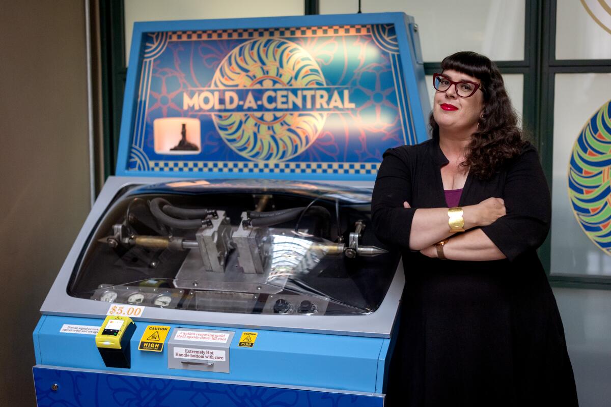 A woman poses for a portrait next to a Mold-A-Rama at the Los Angeles Central Library 