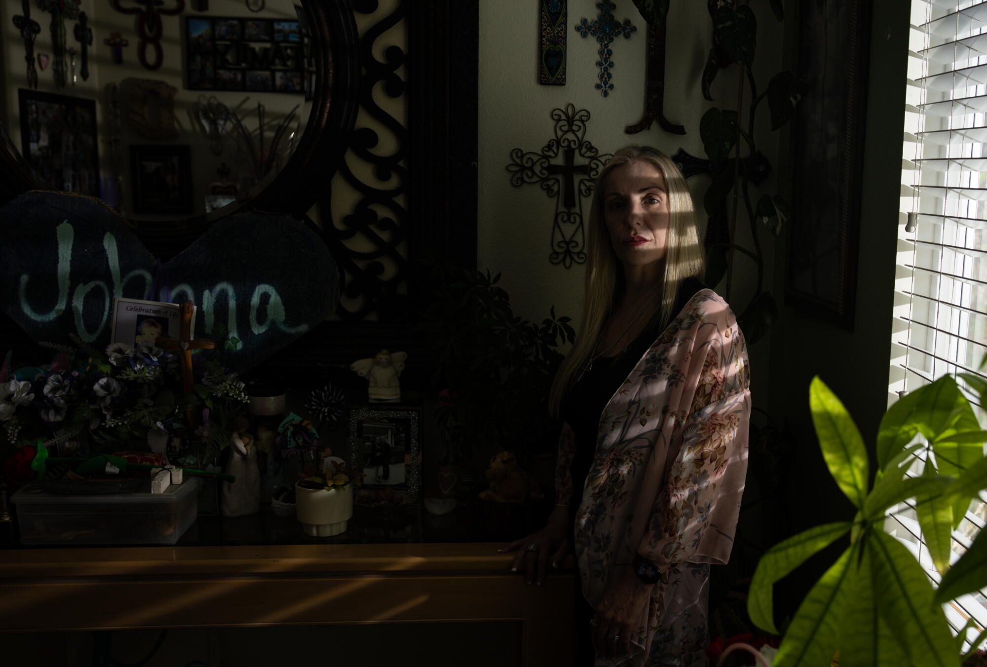 A woman leans with her back to a window inside a home.
