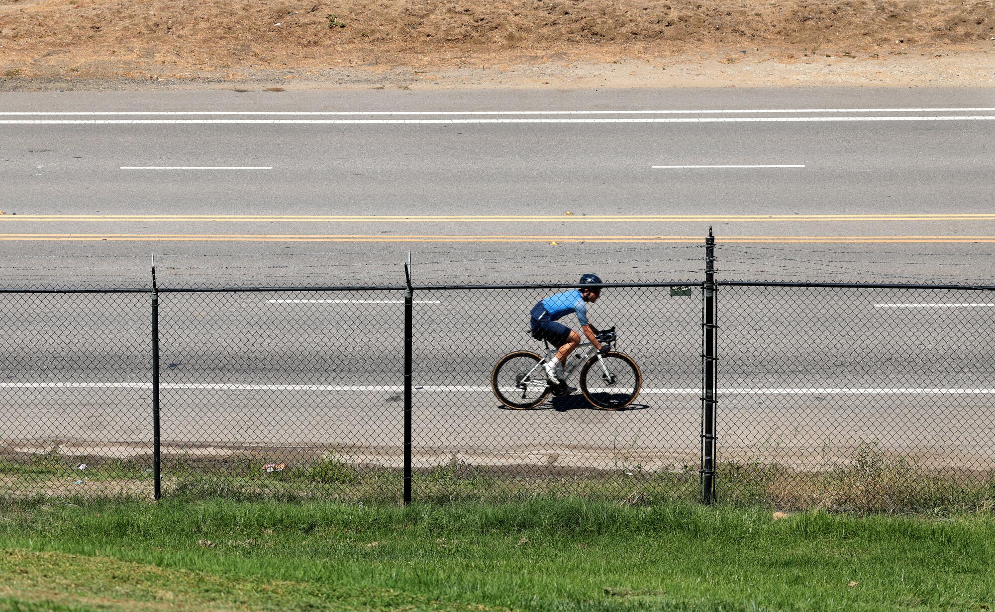 A cyclist rides along a road that is separated from a lawn by a chain-link fence.