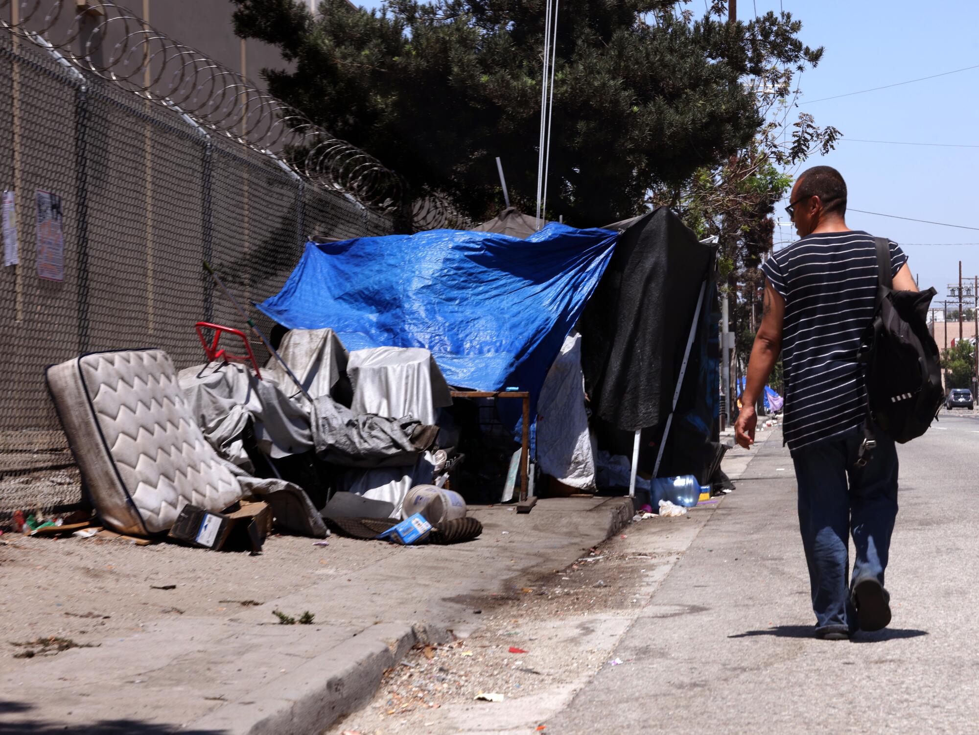 A pedestrian walks into the street to get around a homeless encampment on Alameda Street in downtown Los Angeles.