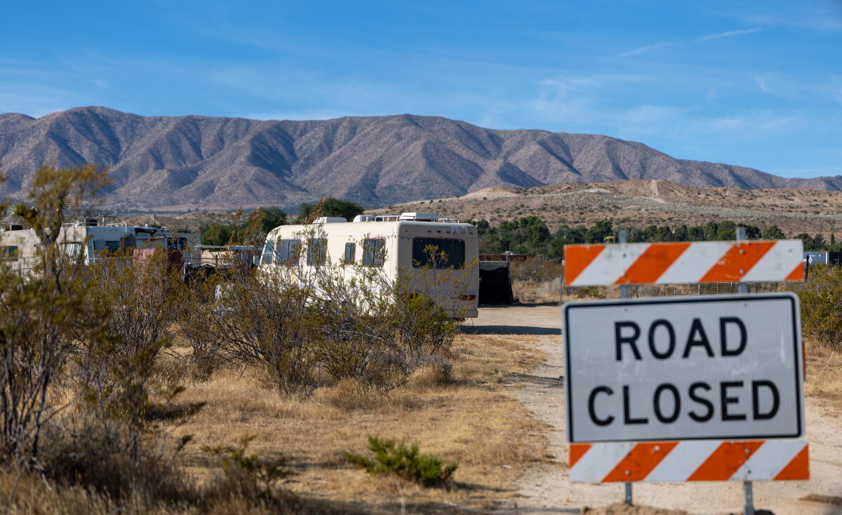 RVs are visible behind a sign that says Road Closed, with mountains in the background