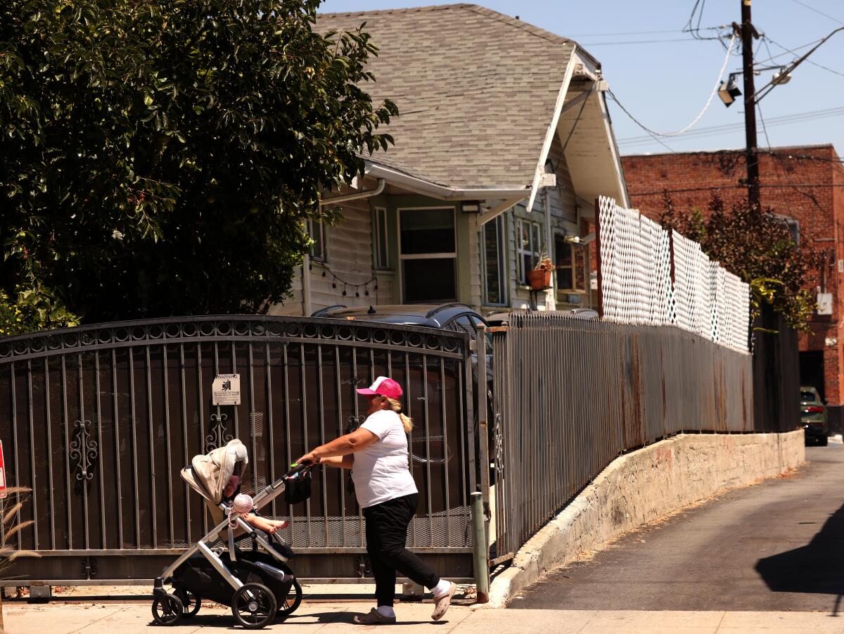 A woman pushes her baby cart past a home that features extended white fencing in the Sunset Square neighborhood in Hollywood.