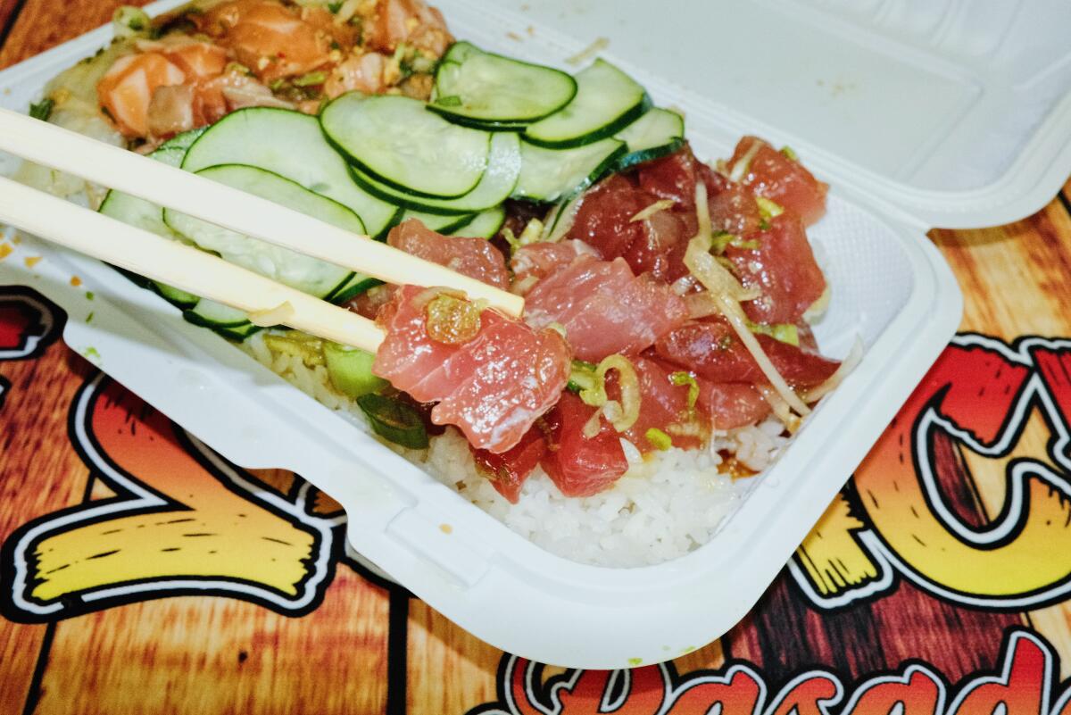 Chopsticks lift raw tuna from a poke bowl in a takeout container