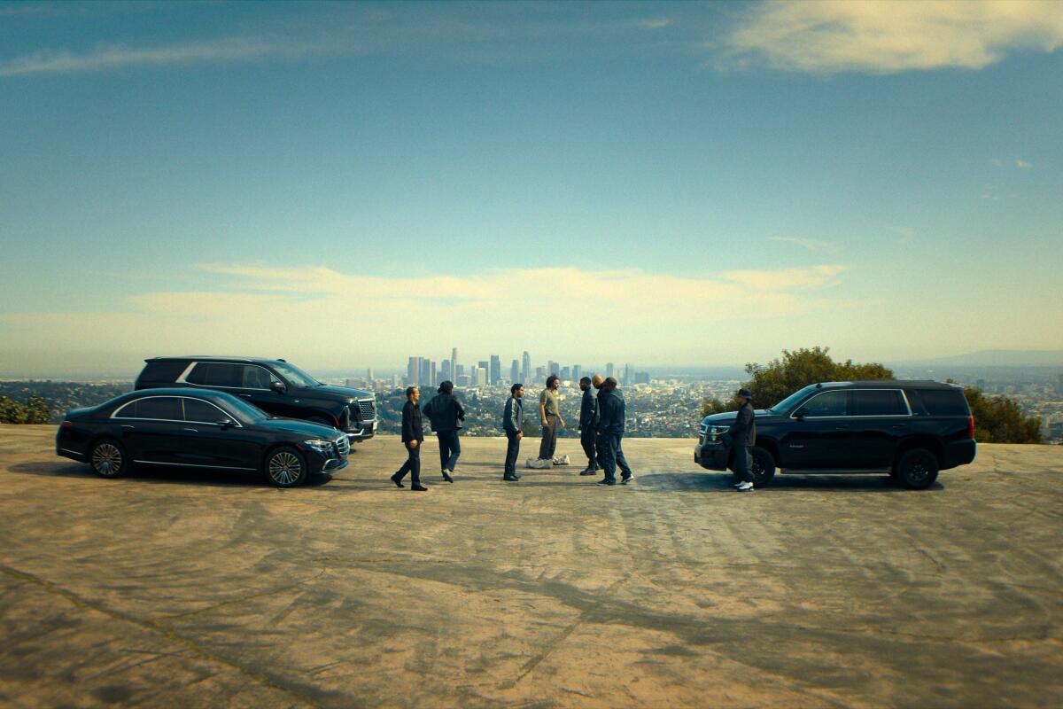 Seven people stand among three vehicles with a city in the background.
