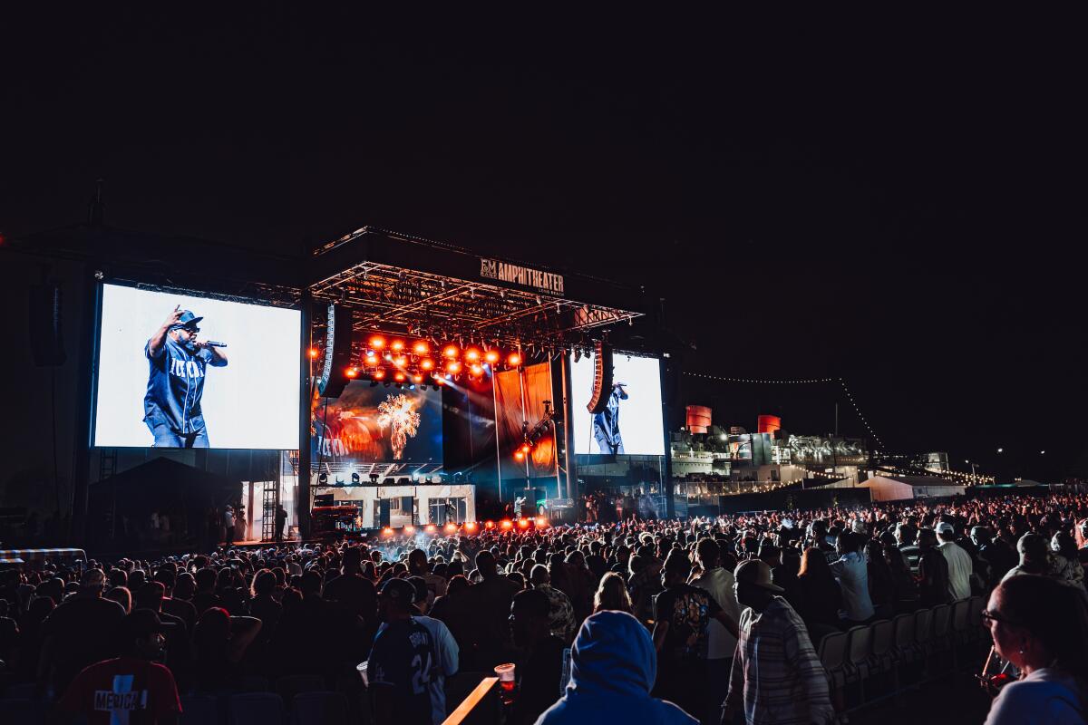 Two big screens show rappers on a stage with lights and a large crowd gathered in front.