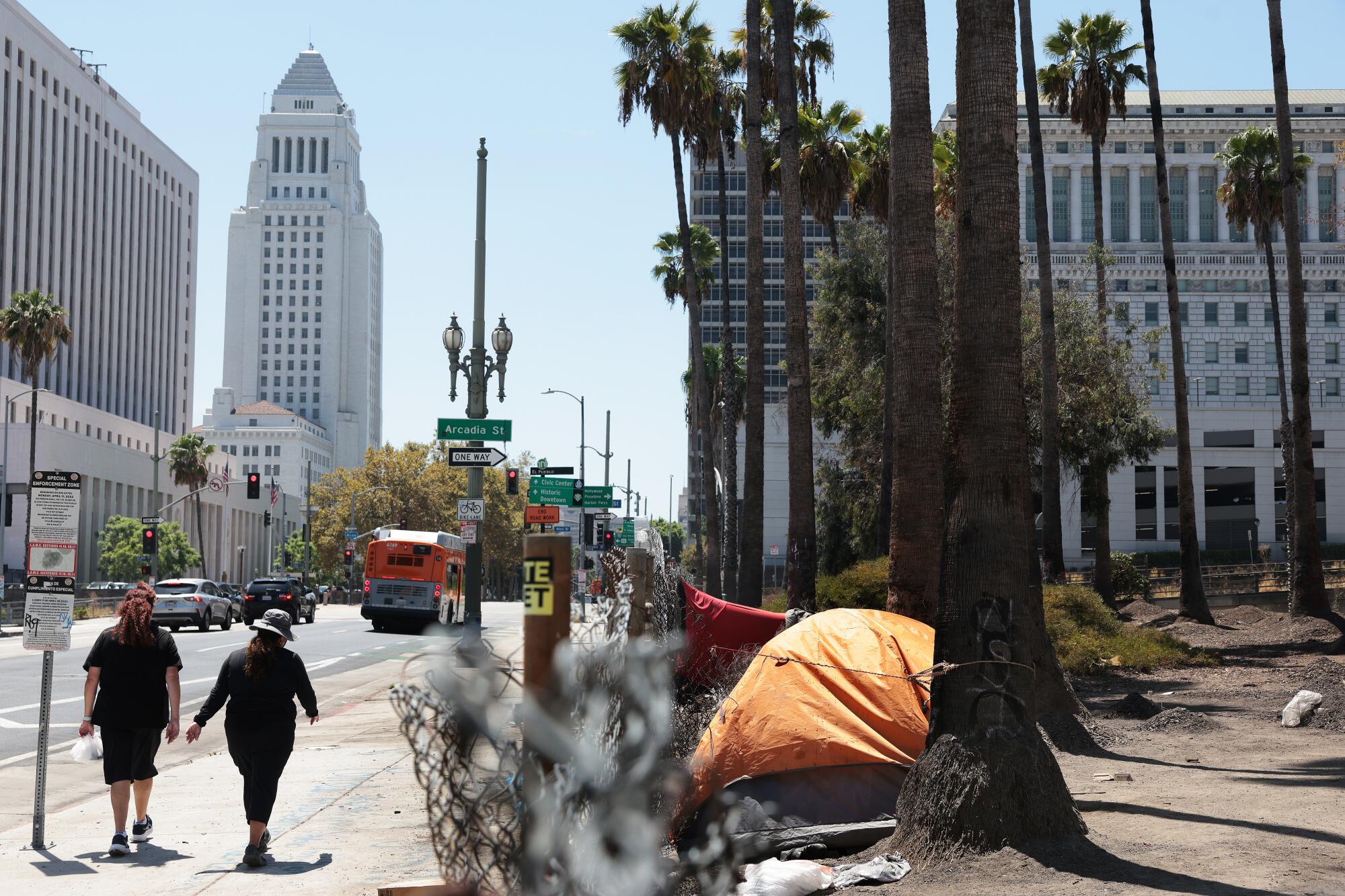 Pedestrians pass by a homeless encampment along the 101 northbound offramp, at right, near City Hall.