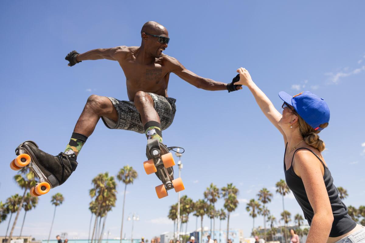 A man in roller skates jumps up and makes a heart symbol with somebody on the ground. 