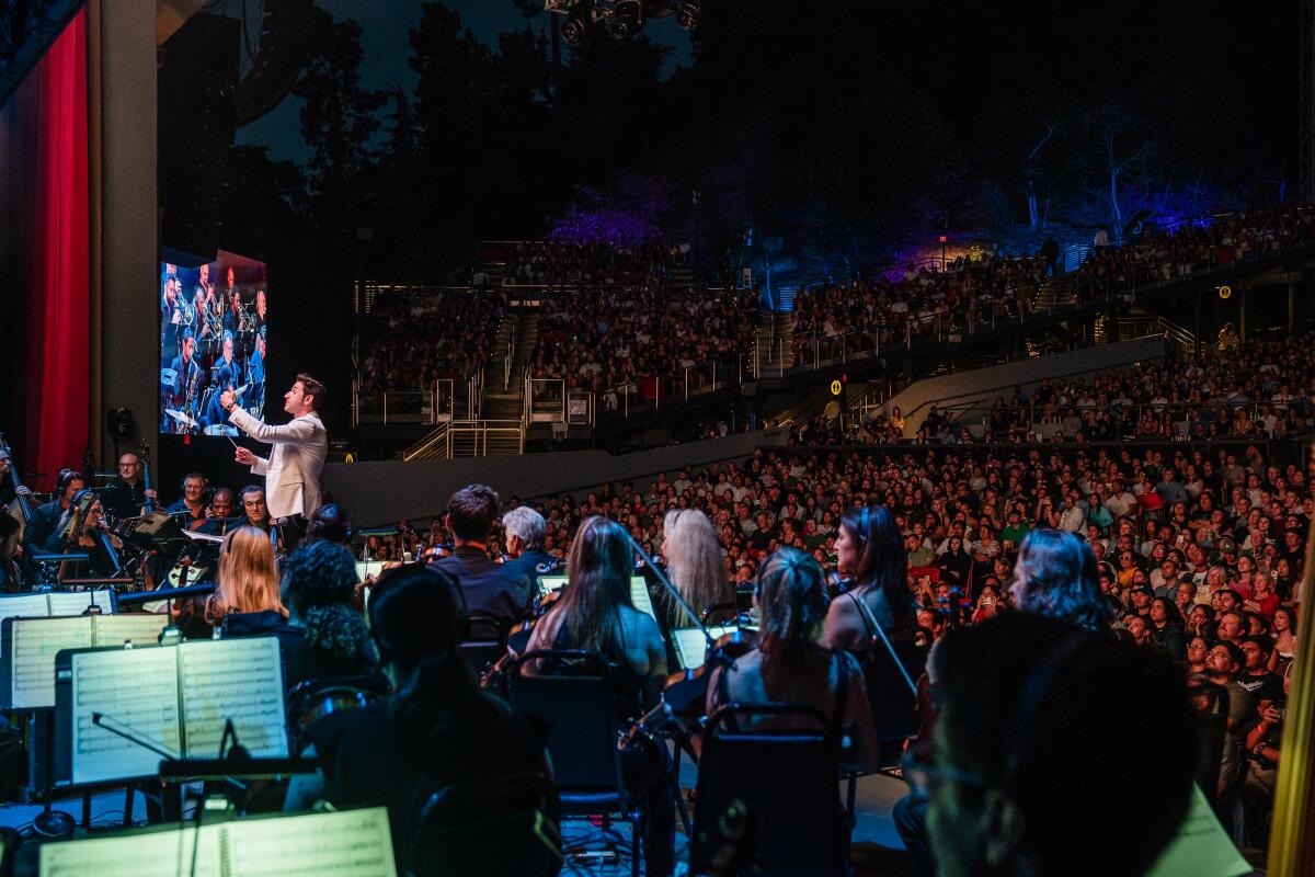 A full audience watches a conductor lead an orchestra.