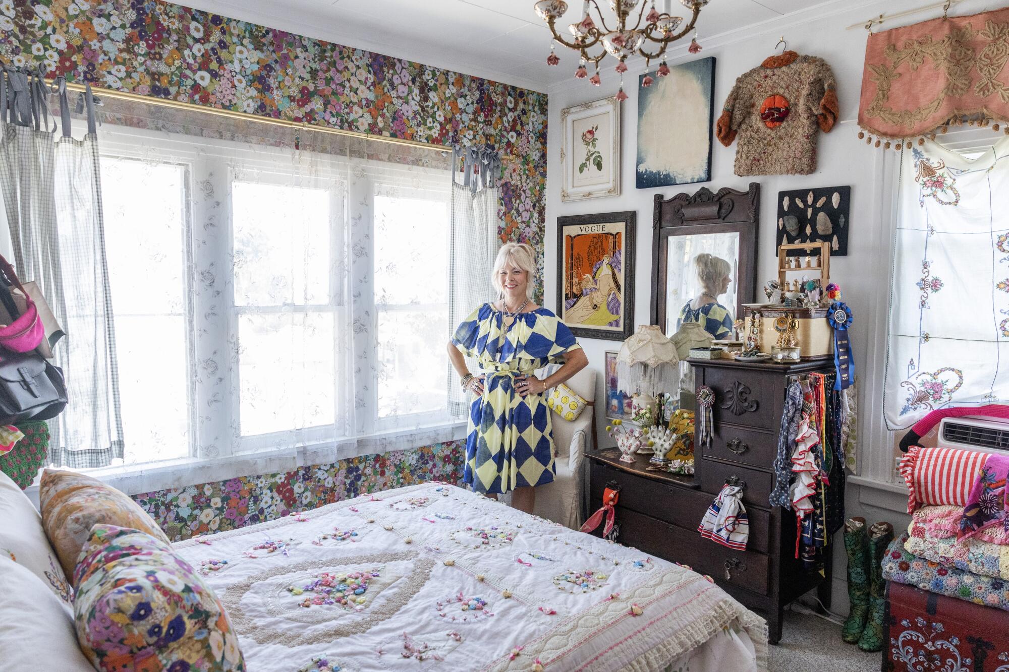 Wendi Weger stands in her bedroom surrounded by art and floral wallpaper.