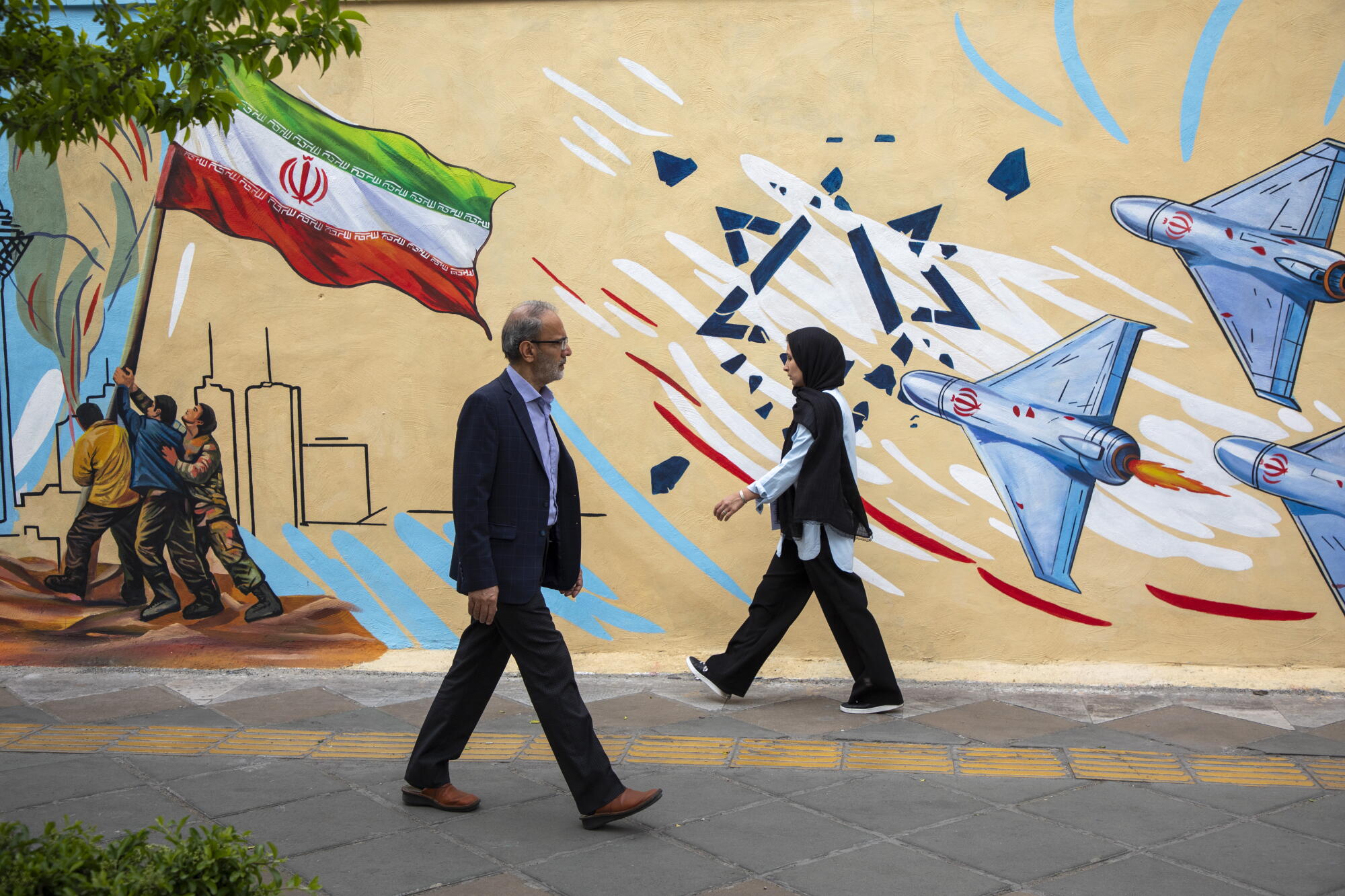 People pass in front of a pro-government political mural in Tehran