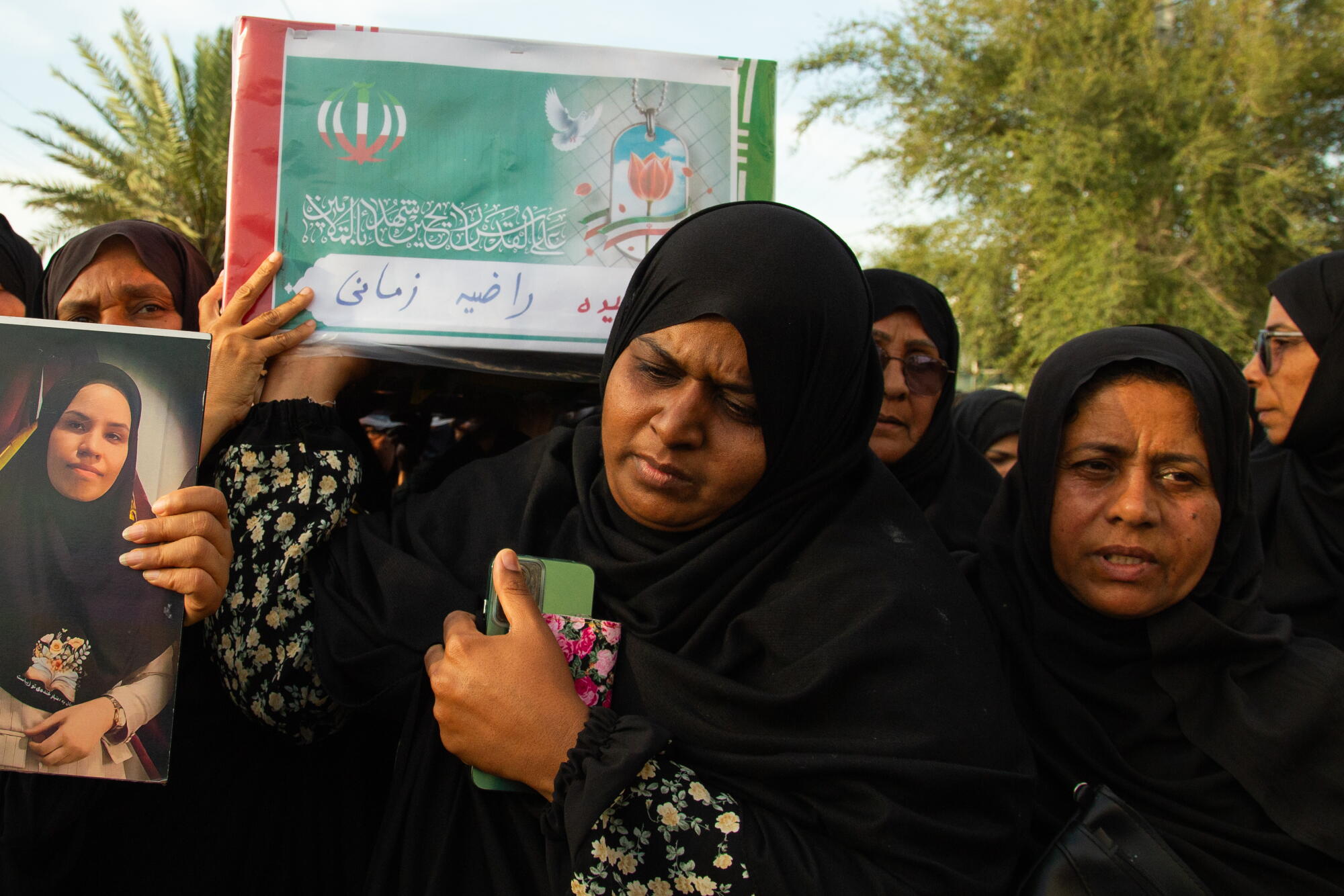 Women in black robes carry a casket 