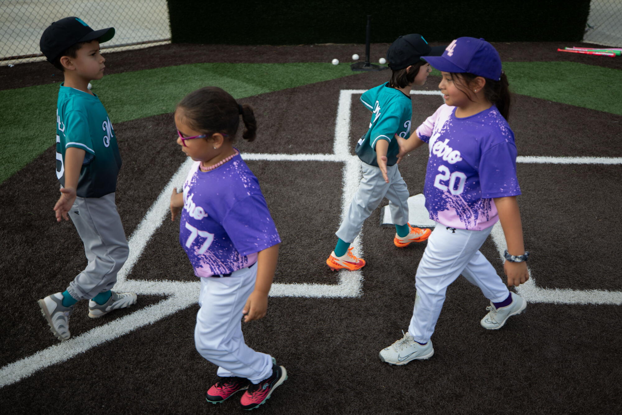 Young children in baseball uniforms slap hands.