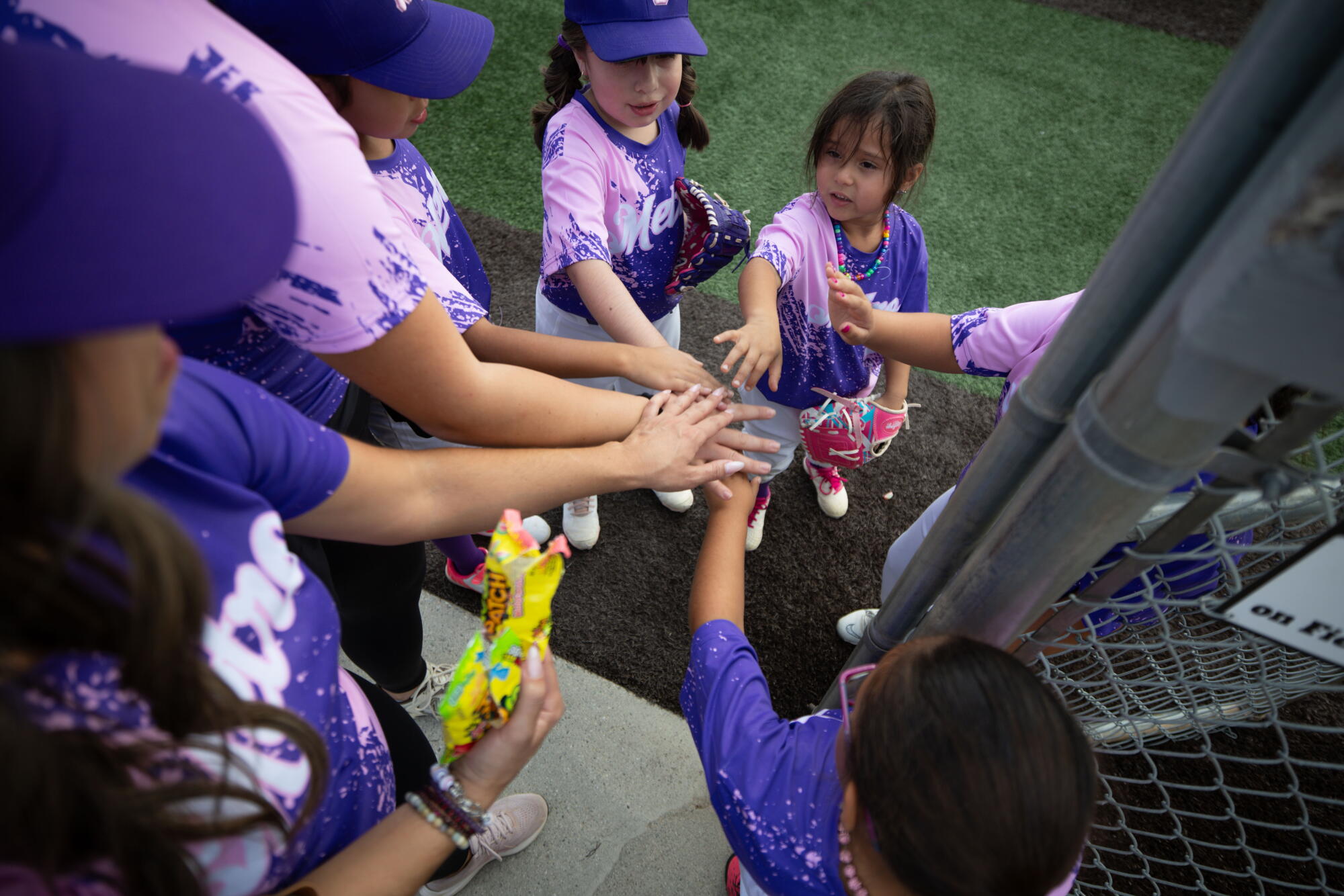 Little League players reach their hands together.