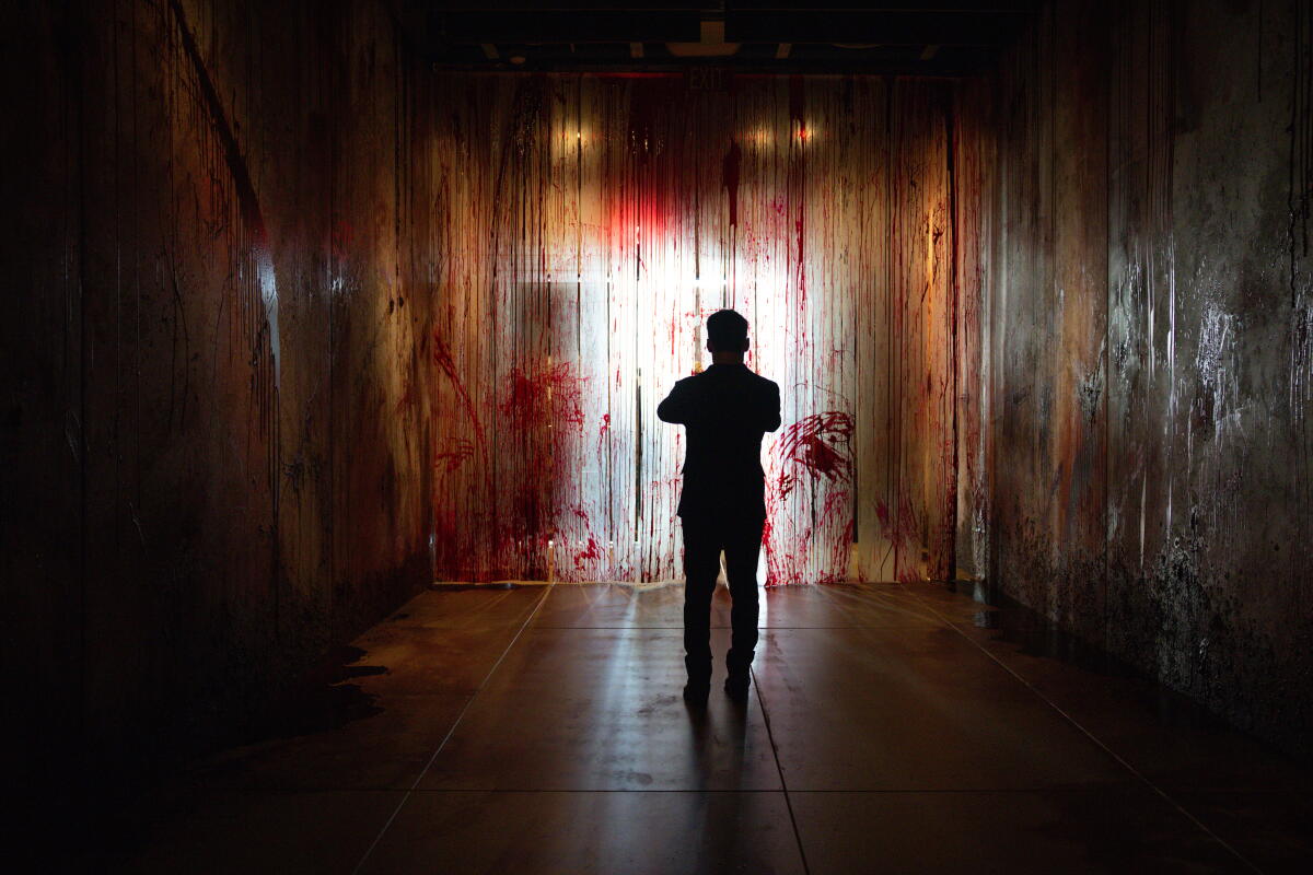 A silhouetted man stands in a room dripping with blood.