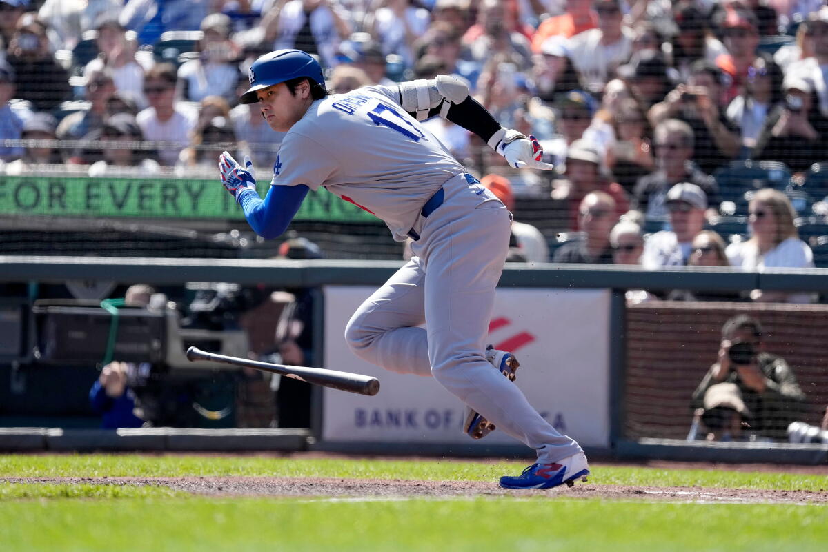 Shohei Ohtani in his Dodgers uniform begins to run with his bat falling to one side.