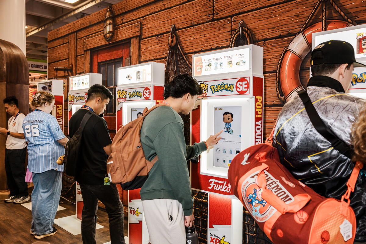 People standing at touch-screen kiosks, designing custom toys