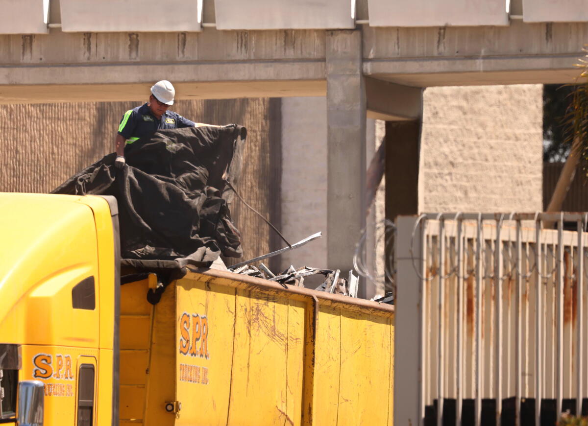 A truck driver places a tarp over scraps of metal that were removed during demolition of the Hawthorne Plaza.
