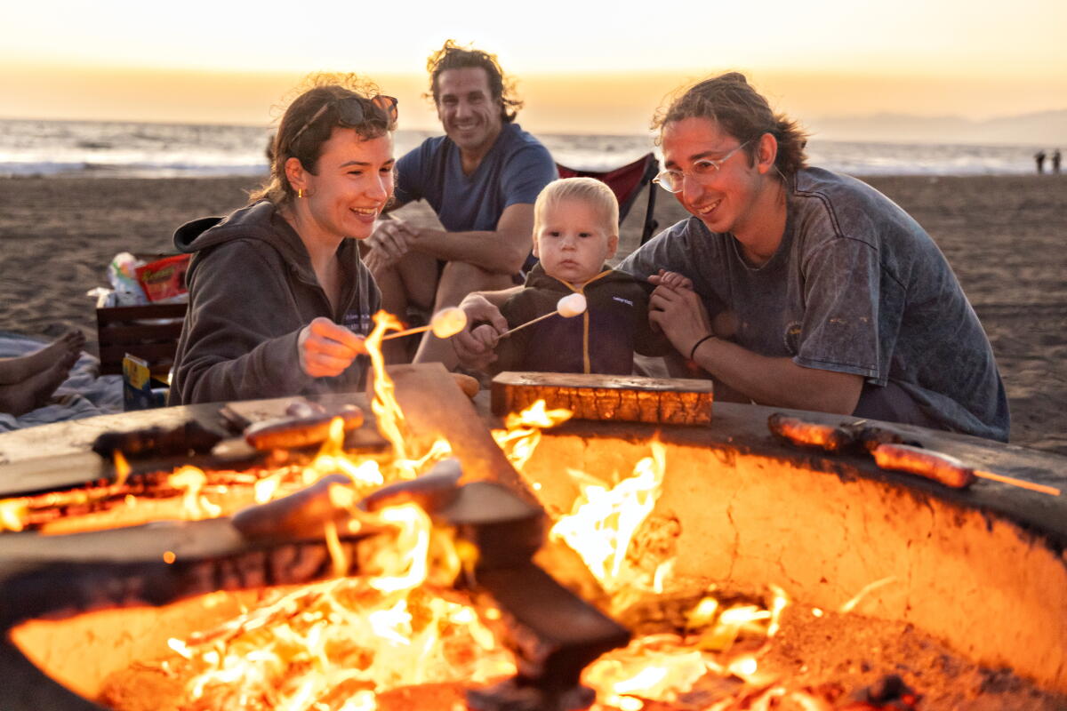 A couple roasts marshmallows at Dockweiler Beach with their son