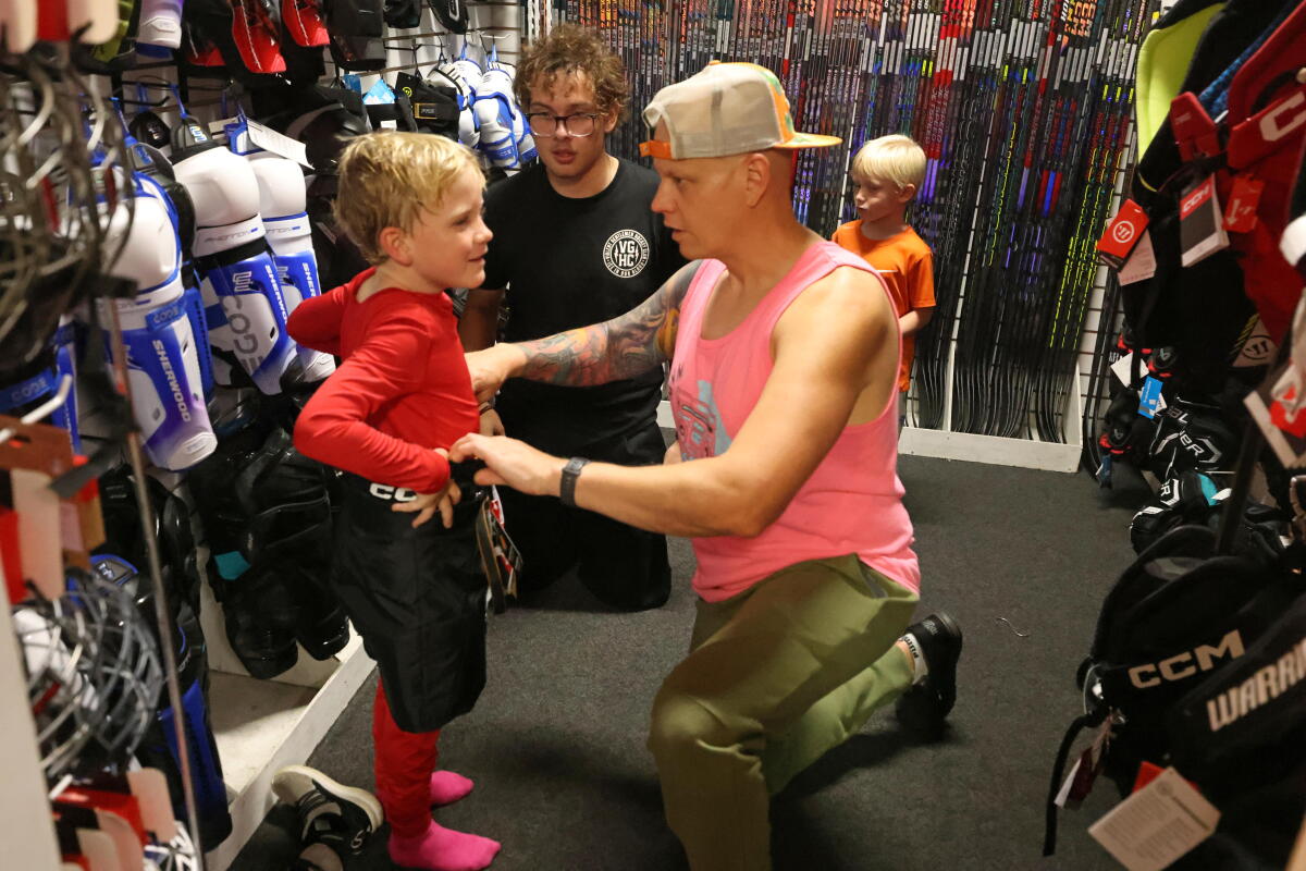 Sean Zabriskie, center, helps his son Connor, 7, try on hockey pants