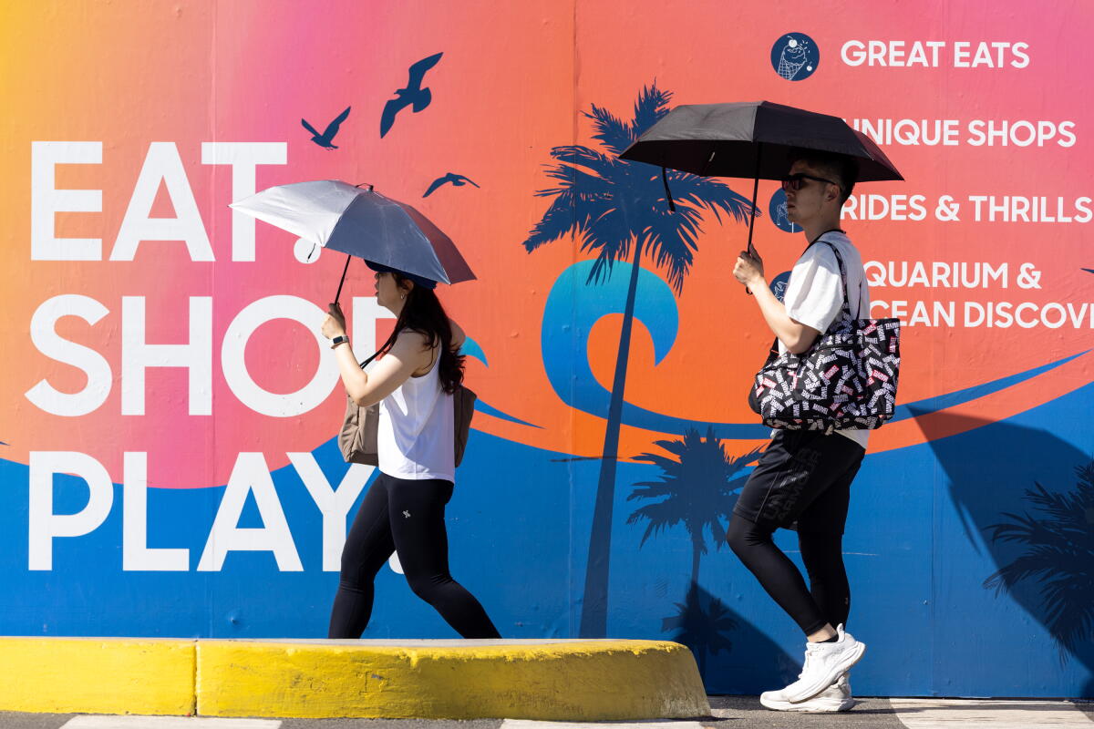 People walk with umbrellas to shade from the heat at the Santa Monica Pier on Aug. 24 in Santa Monica.